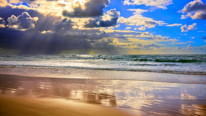 Beach with sunbeams through clouds over the ocean