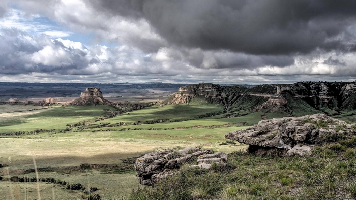 Rocky buttes and green fields under cloudy sky