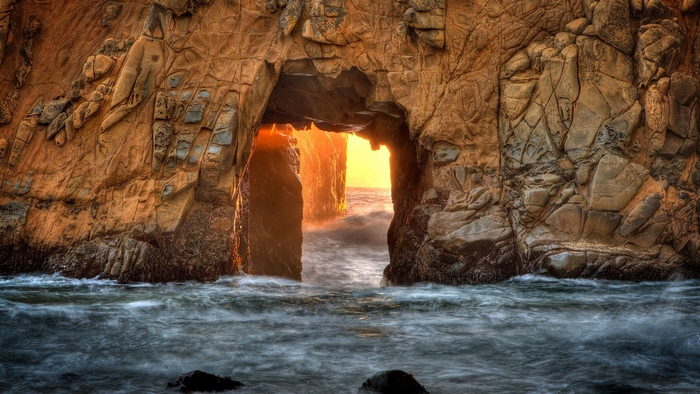 Ocean waves crashing through a rock arch at sunset