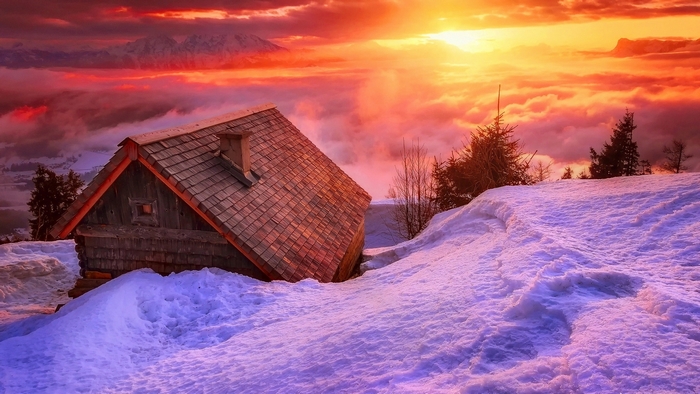 Wooden hut in snowy mountains at sunset