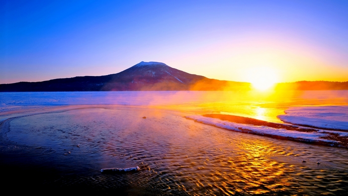 Sunrise over a misty mountain lake with snow