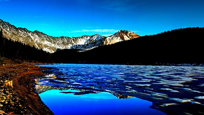 Snow-capped mountains reflected in a partially frozen lake