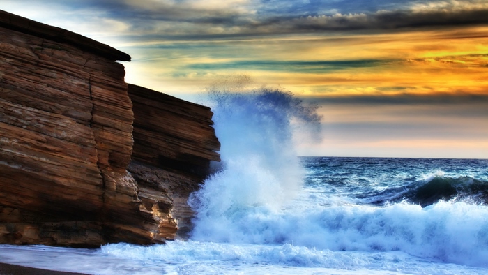 Waves crashing against rocky cliffs at sunset