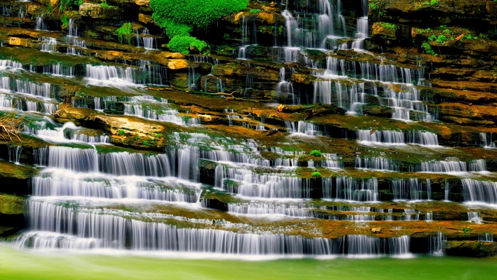 Tiered waterfall cascading over layered rocks with green plants