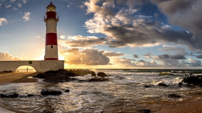 Red and white lighthouse on a rocky coast at sunset