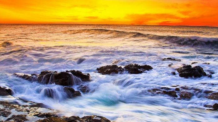 Ocean waves crashing on rocks at sunset