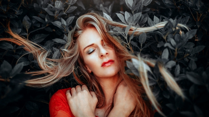 Serene Woman with Flowing Hair Among Dark Leaves