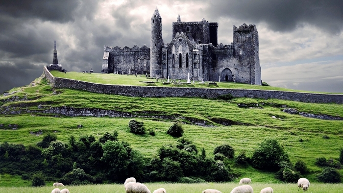 Castle on a grassy hill with sheep and stormy clouds