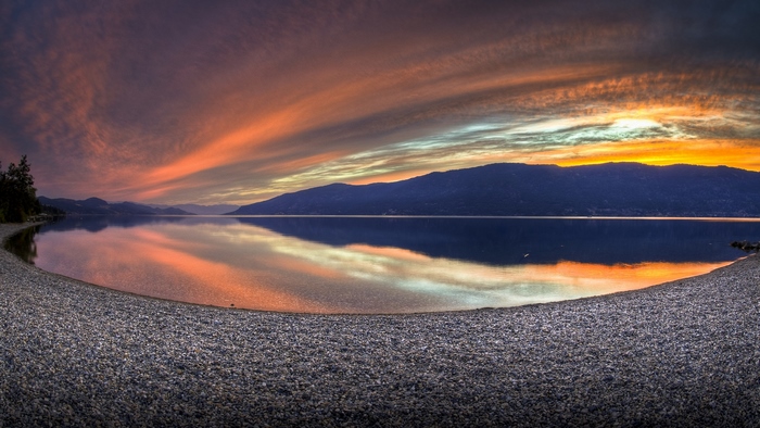 Sunset over a calm lake with mountains and a pebble beach