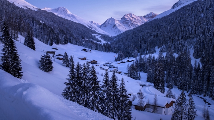 Snowy mountain valley with houses and pine trees