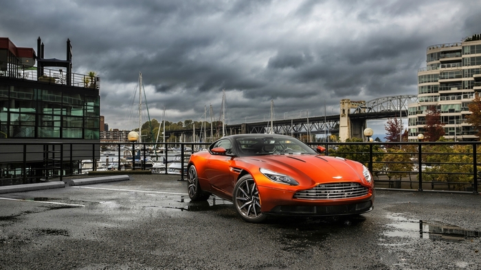 Orange Aston Martin DB11 parked by a marina
