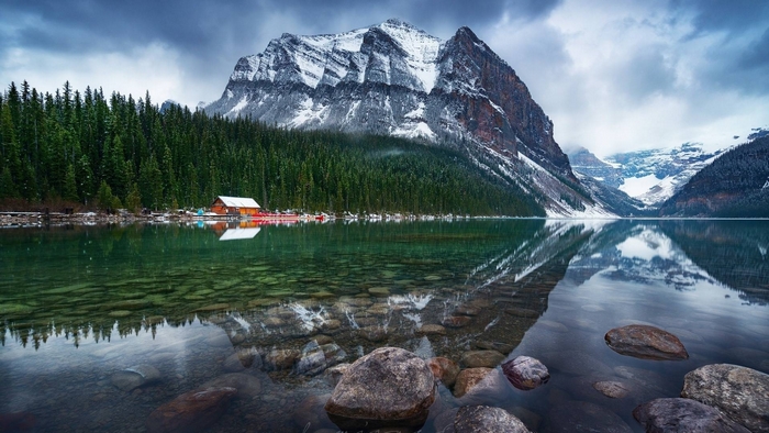 Snow-capped mountain reflected in a clear lake with a forest and cabin