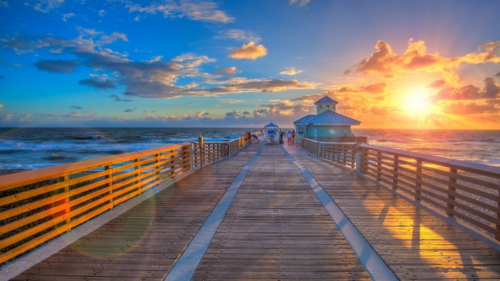 Sunrise over a wooden pier with ocean waves and clouds
