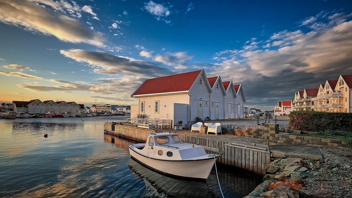 Boat docked in a harbor with houses and clouds