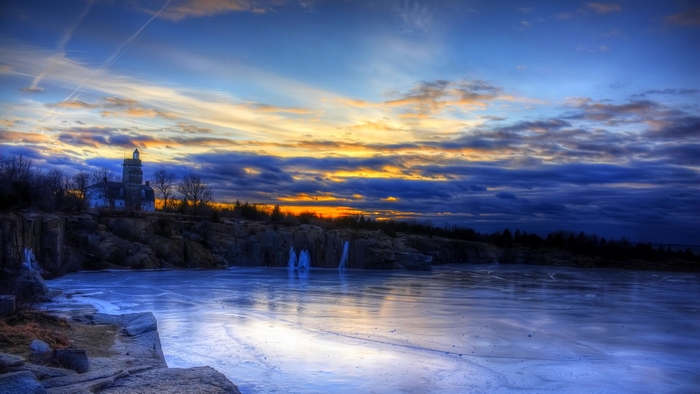 Lighthouse on a rocky coast during sunset with frozen water