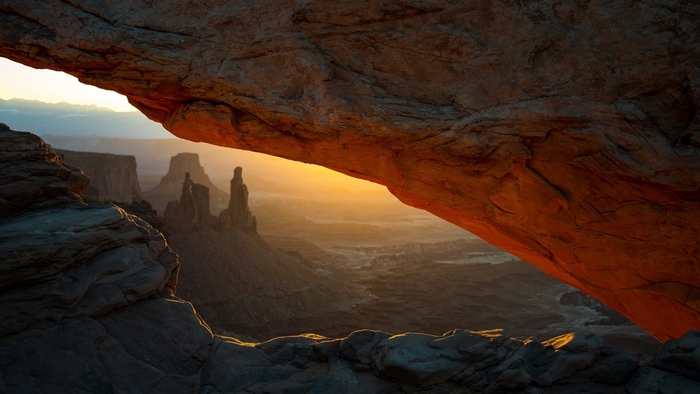 Sunrise over a desert canyon viewed through a rock arch