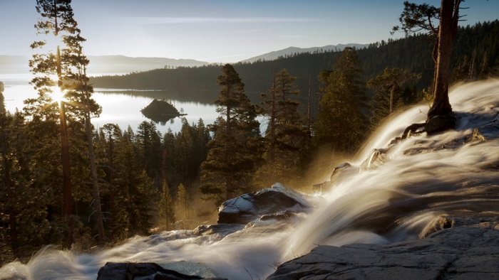 Waterfall flowing into a lake at sunrise with mountains