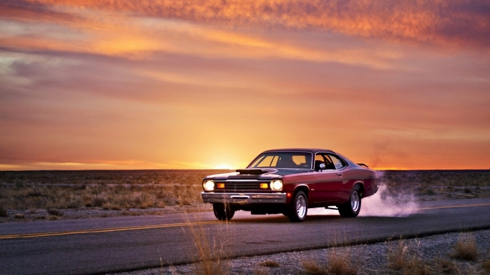Red Plymouth muscle car drifting at sunset