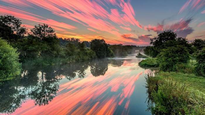 River reflecting pink clouds and trees at sunset