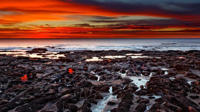 Rocky beach at sunset with vibrant orange clouds over the ocean