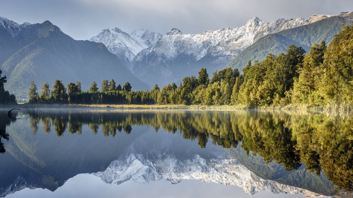 Snow-capped mountains reflected in a calm lake with trees