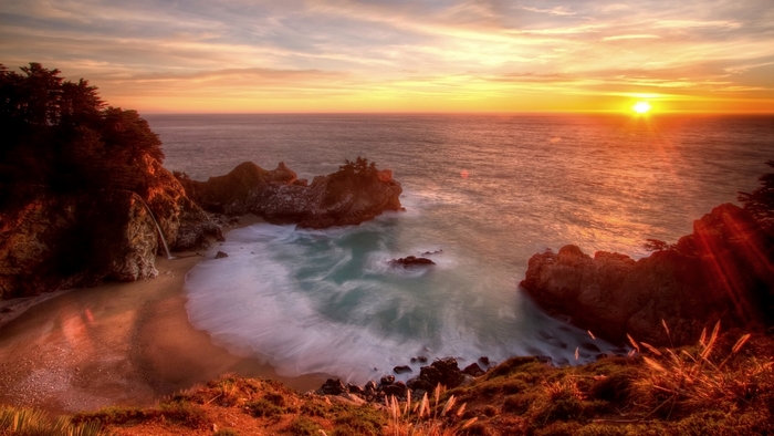 Sunset over a rocky coast with a waterfall and beach