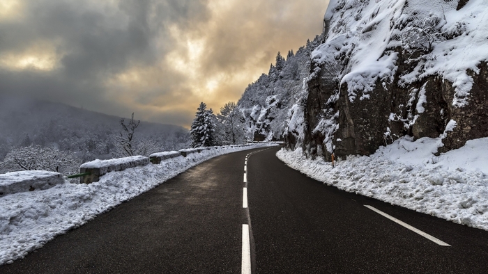Winding mountain road covered in snow under cloudy sky