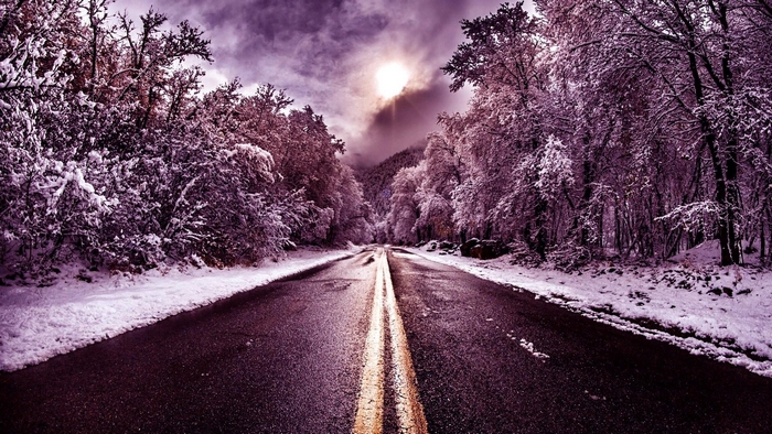 Road through a snow-covered forest with sun and clouds