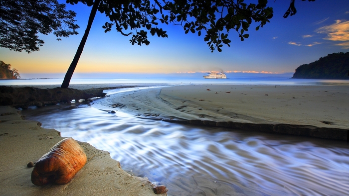 Beach with stream and cruise ship at sunset
