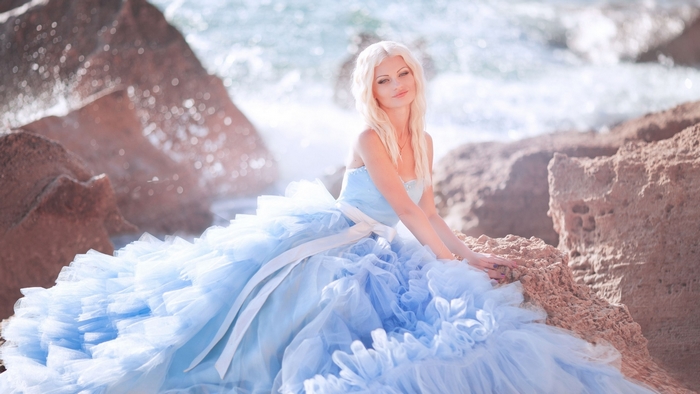Woman in a blue dress on rocks by the sea