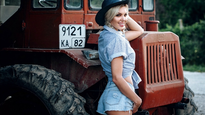 Woman in shorts and hat leaning on a tractor