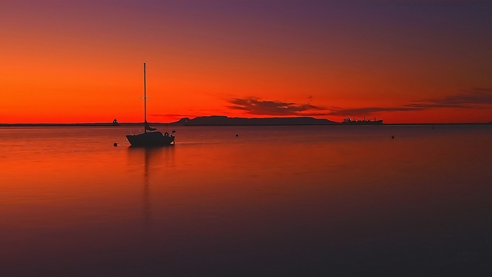 Sailboat drifting on calm water at sunset