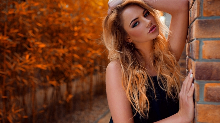 Blonde woman leaning against a brick wall