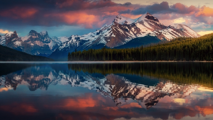 Snow-capped mountains reflected in a calm lake in Alberta, Canada