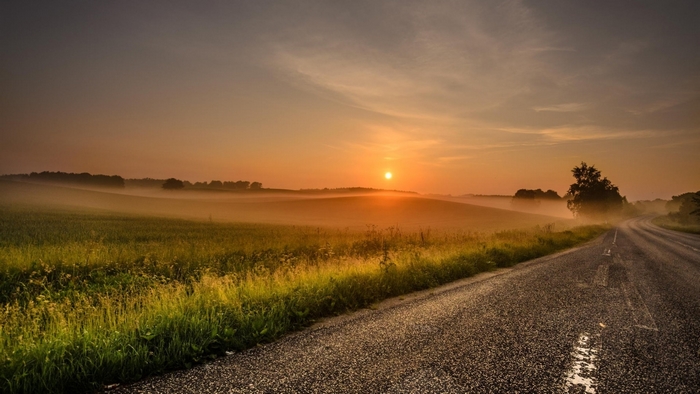 Sunrise over a misty rural landscape with a road
