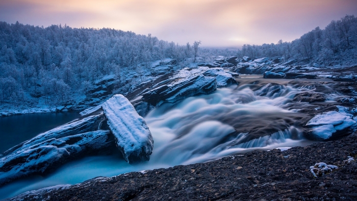 Winter waterfall flowing over rocks with snow-covered trees