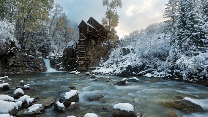 Old wooden mill on a cliff by a river in winter
