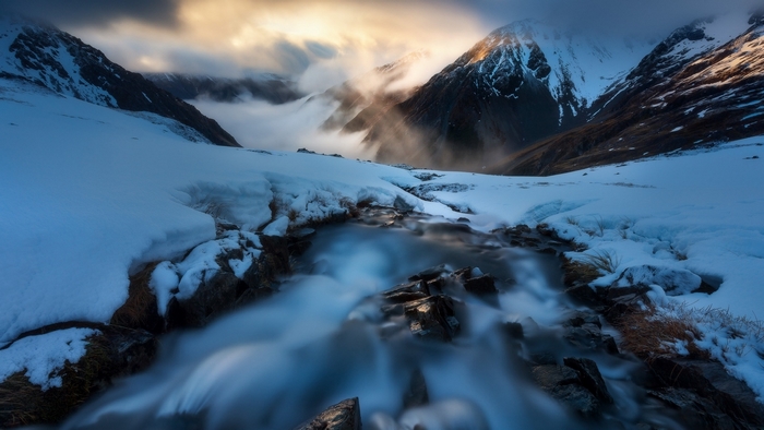 Snowy mountains with a stream and dramatic clouds
