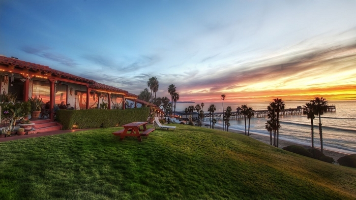 Coastal house with pier and palm trees at sunset
