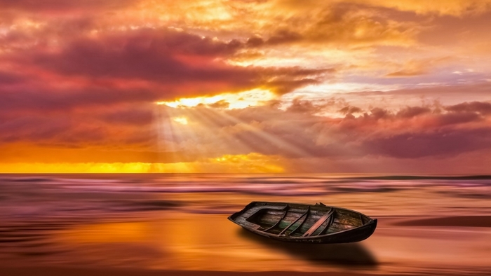 Boat on a beach at sunset with sunbeams
