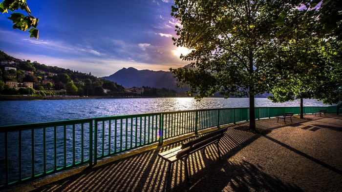 Lakeside promenade with trees and mountains at sunrise