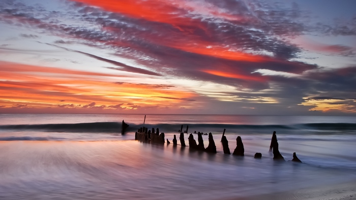Shipwreck remains on a beach at sunrise with colorful clouds