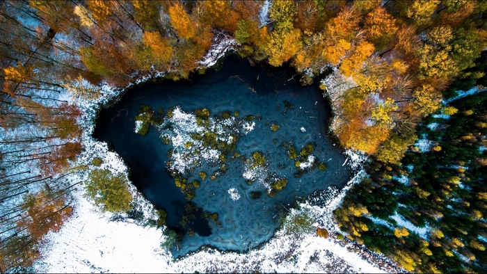 Aerial view of a lake surrounded by autumn trees and snow