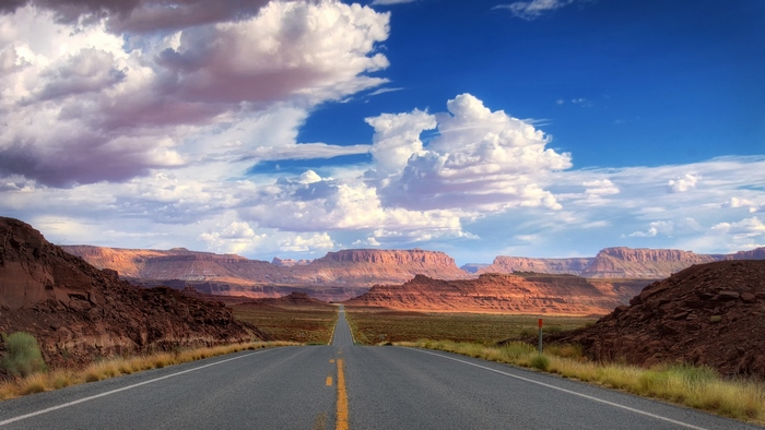 Desert road with mesas and clouds