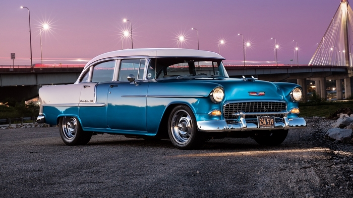 Blue and white 1955 Chevrolet Bel Air parked by a bridge at dusk