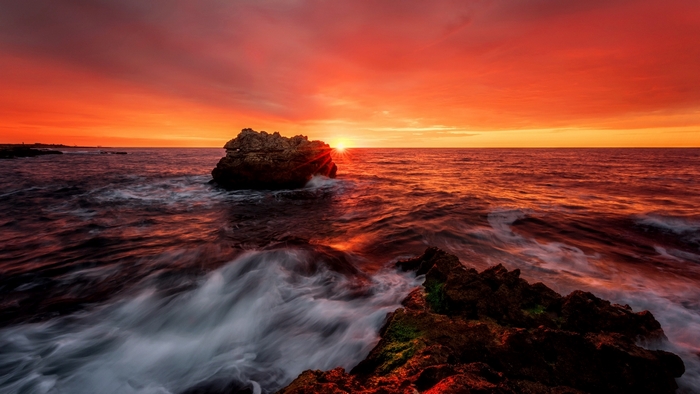 Sunset over the sea with waves crashing on rocks