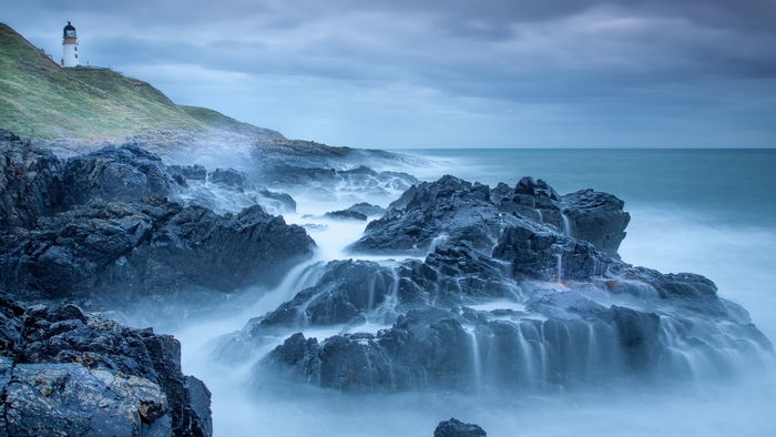 Lighthouse on a rocky coastline with waves crashing