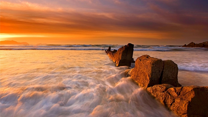 Ocean waves crashing on rocks at sunrise
