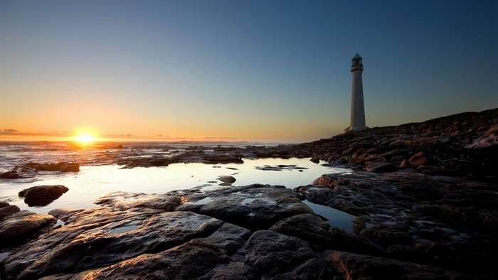 Sunset over the ocean with a lighthouse on the coast