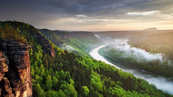 Misty river valley with forested mountains at sunrise